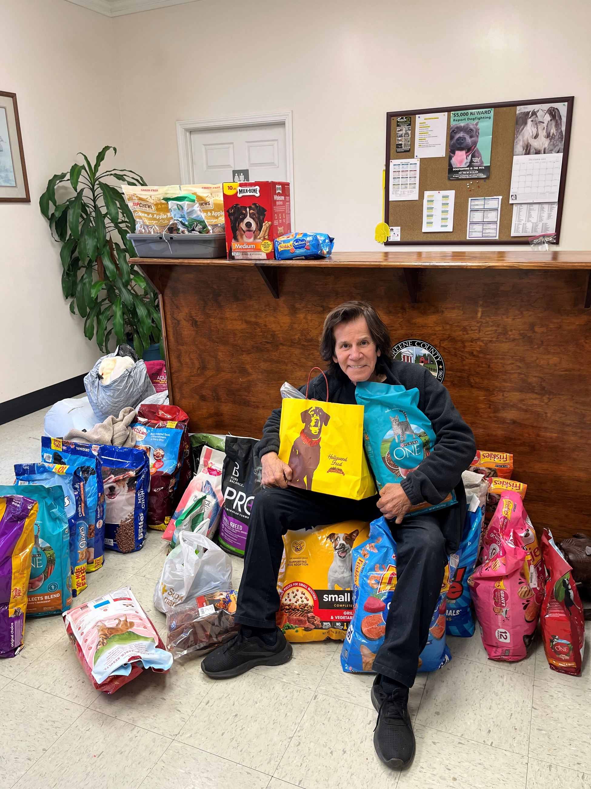Man sitting amongst dog and cat food bags along with trash bags full of donations.