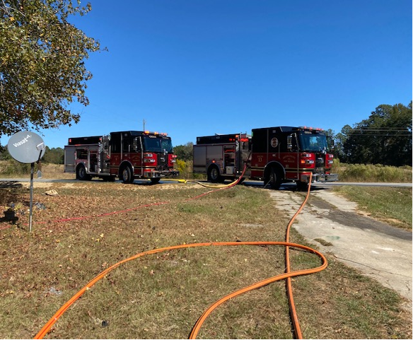Two fire trucks with hoses stretched out across the grass