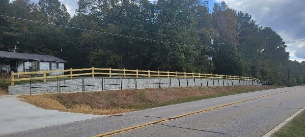 Concrete walking path between a retaining wall and a metal fence next to a road. 