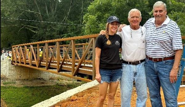 Three people standing in front of an iron bridge. 