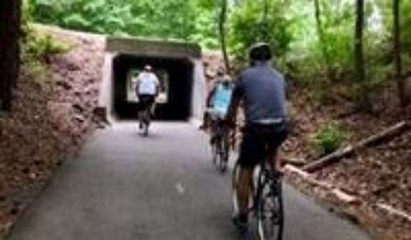 Three bike riders on a concrete path going into a tunnel. 