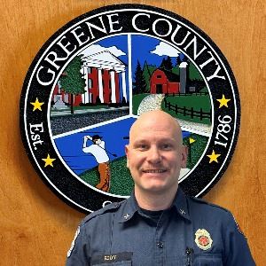 Christopher Eddy standing in front of the Greene County Logo